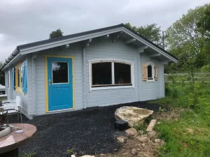 Single-storey log cabin with blue trim and landscaped garden